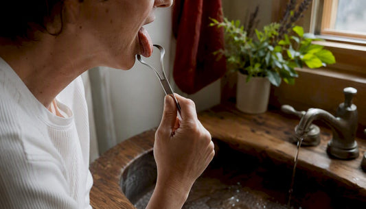 Hand using tongue scraper above sink