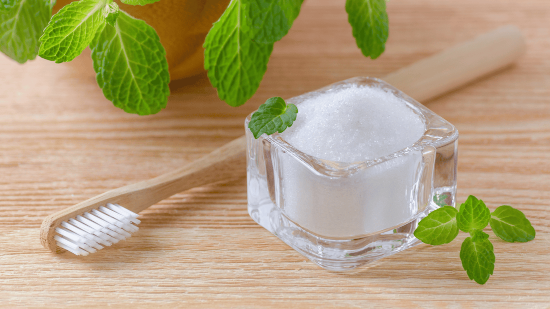 Natural toothpaste in a glass container with a bamboo toothbrush, surrounded by fresh mint leaves on a wooden surface.